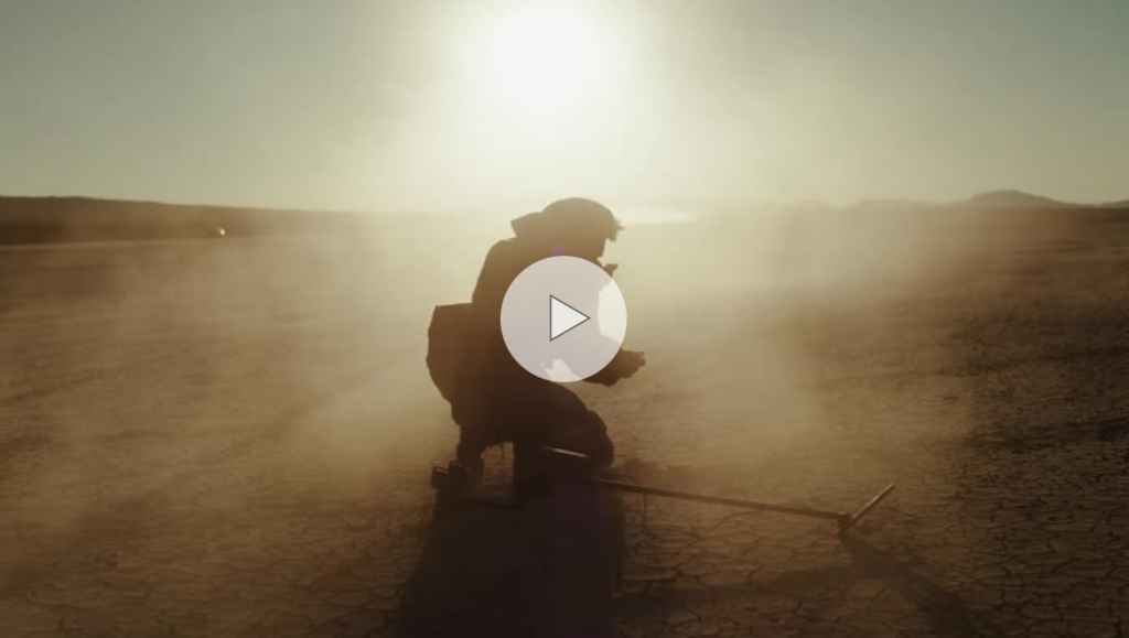 Man holding a metal detection device and finding an object on dry desert ground.